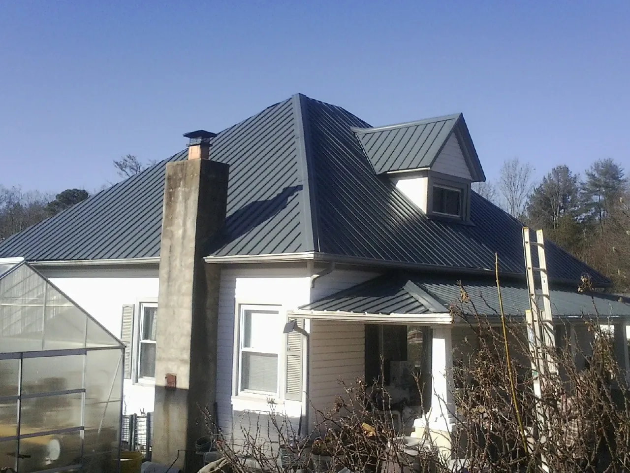 Dark blue standing seam metal roof on a white farmhouse with dormer — Slate & Tile Roof Repair by Roofing Brothers in Lyndeborough