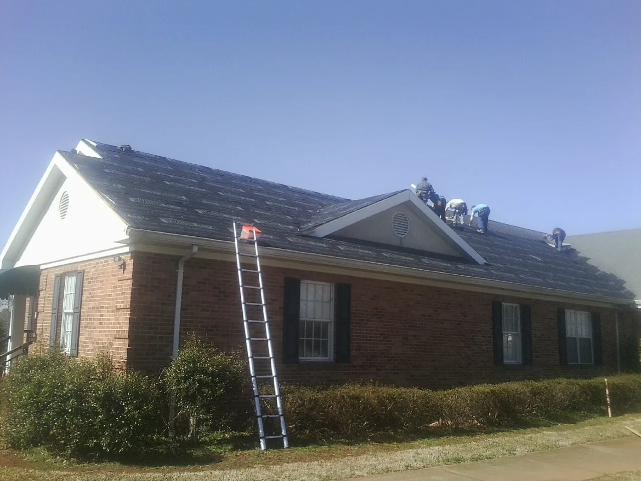 Crew tearing shingles off a brick ranch roof with a ladder set — Metal Roof Repair work by our crew in Lyndeborough