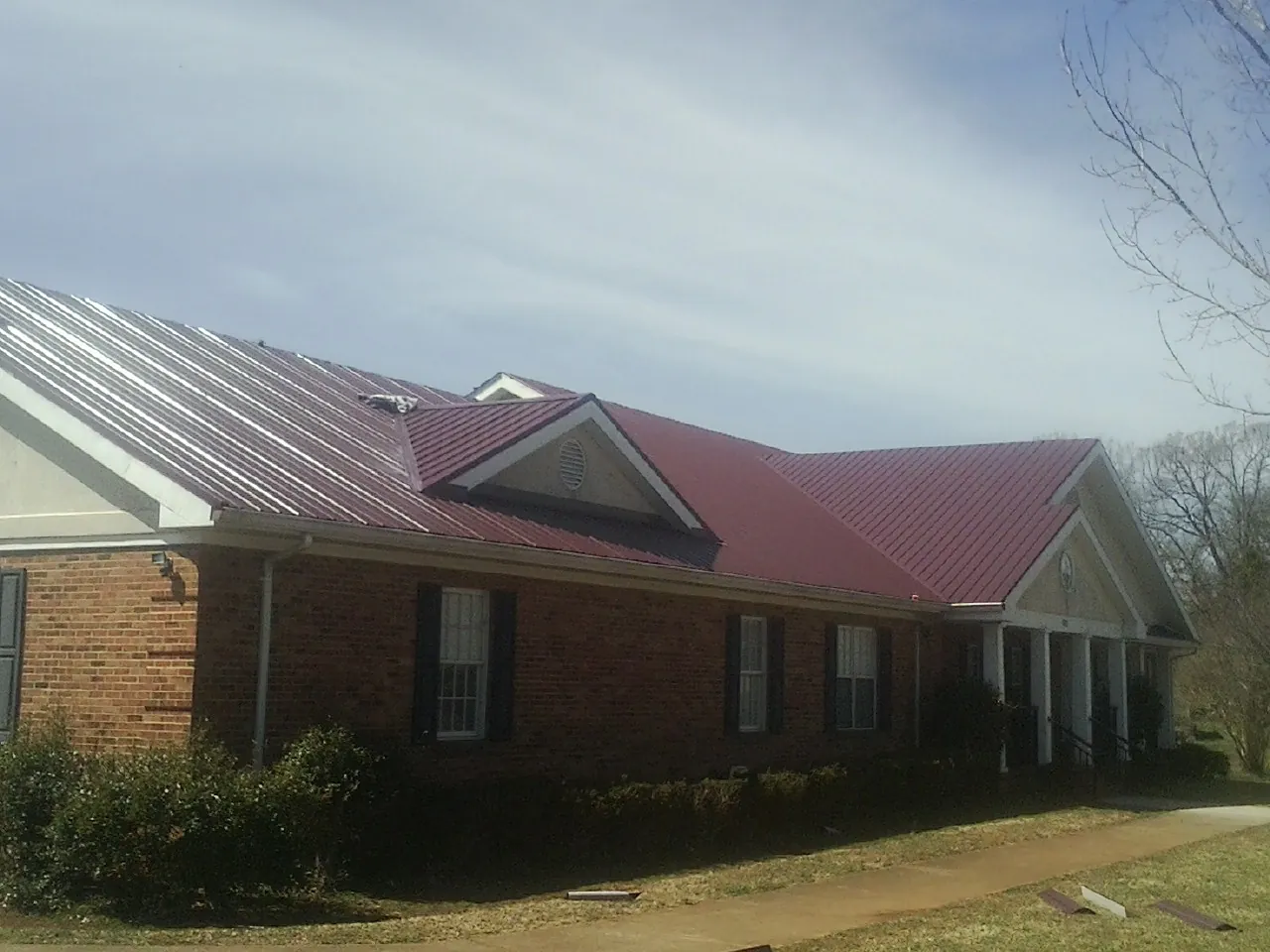Red metal roof with gabled entries on a long brick building, from a Hail Damage Roof Repair job in Lyndeborough
