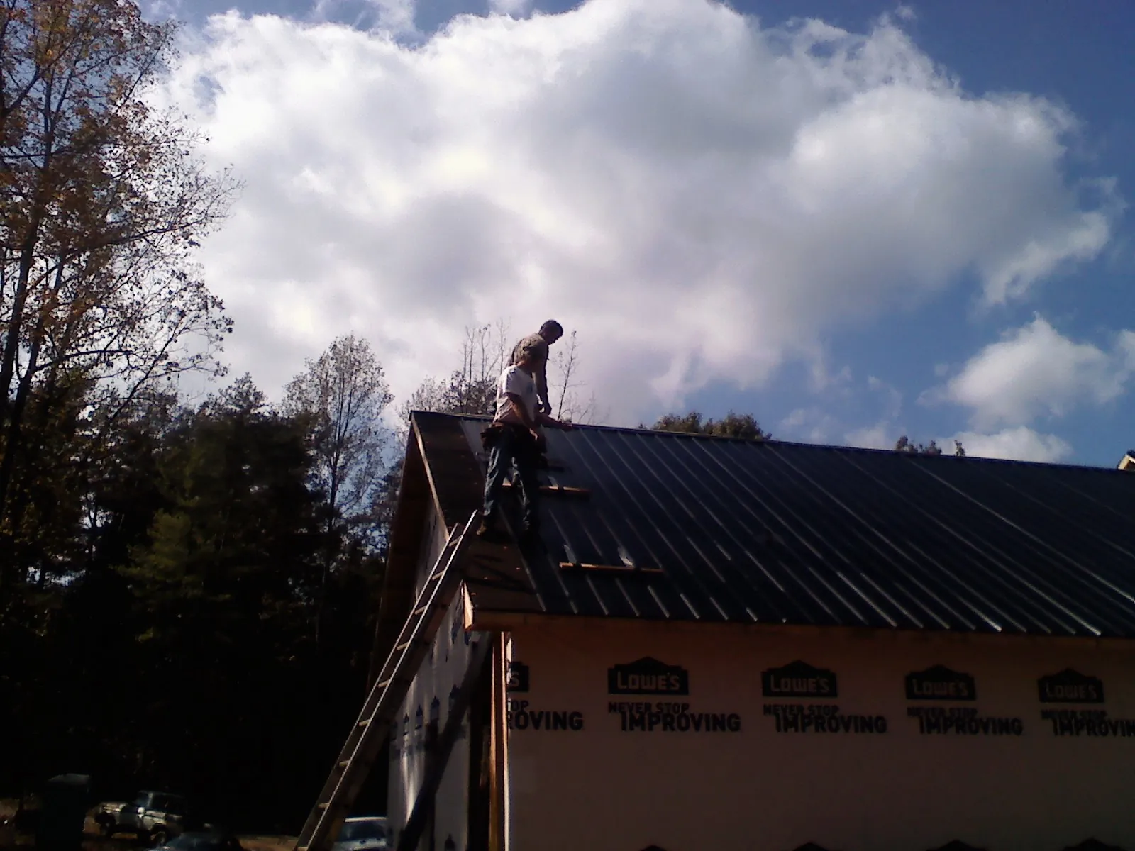 Roofer fastening dark metal panels high against a cloudy sky, from a Roof Inspection job in Lyndeborough