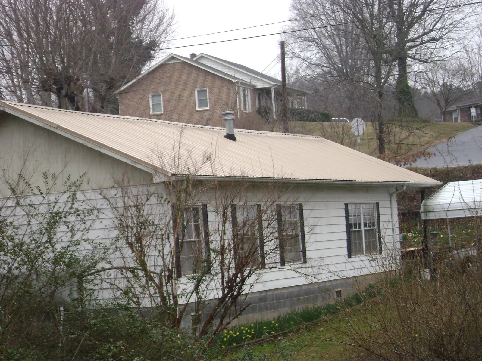 Tan metal roof on a white sided house set into a hillside — Commercial Roofing by Roofing Brothers in Lyndeborough