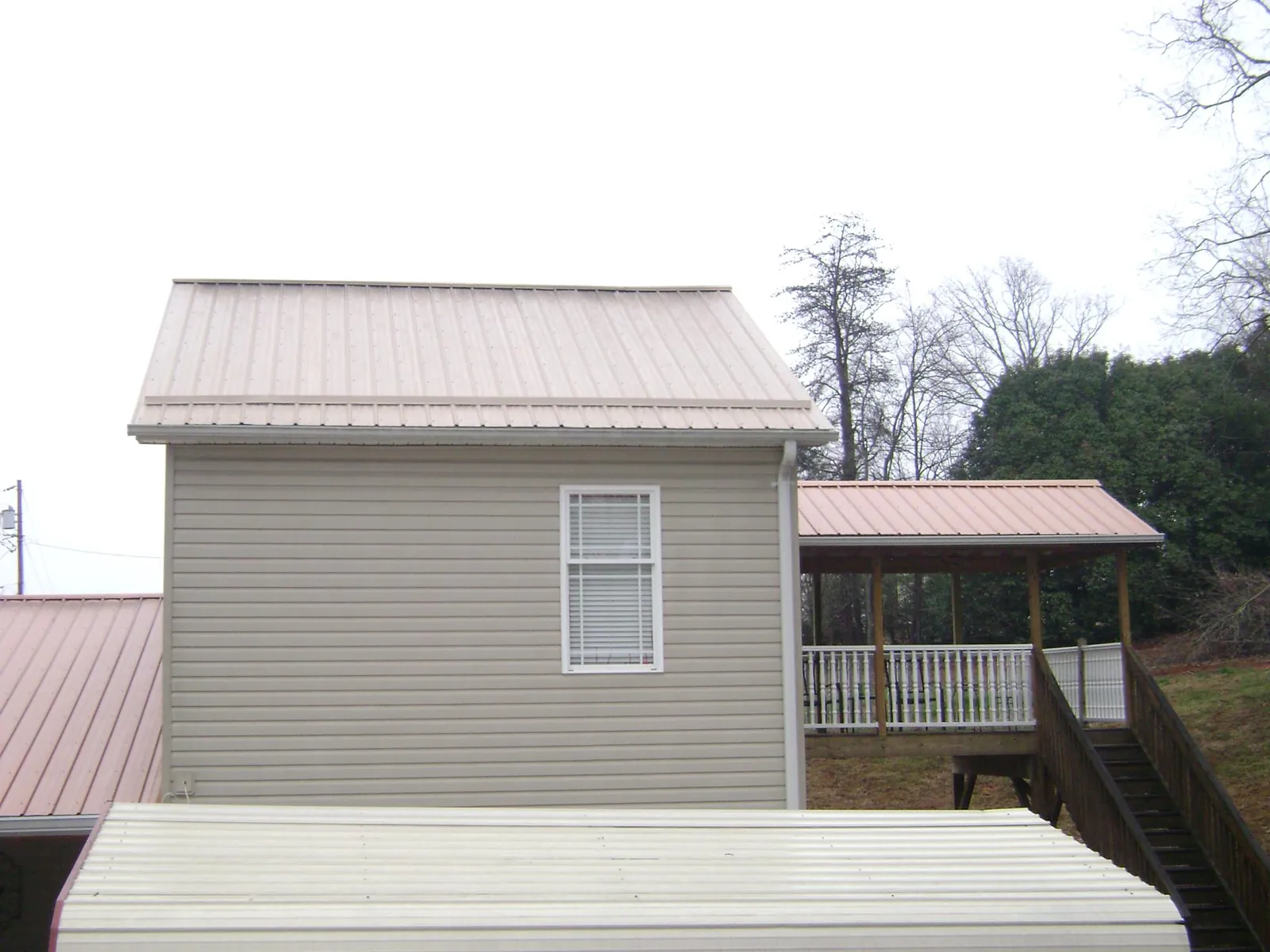 Tan metal roofs on a two story addition and attached porch, from a Roof Replacement job in Lyndeborough